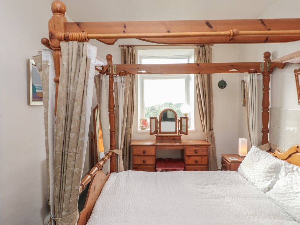 A bedroom with a four-poster bed and a dressing table at King Arthur Suite in Trearddur Bay