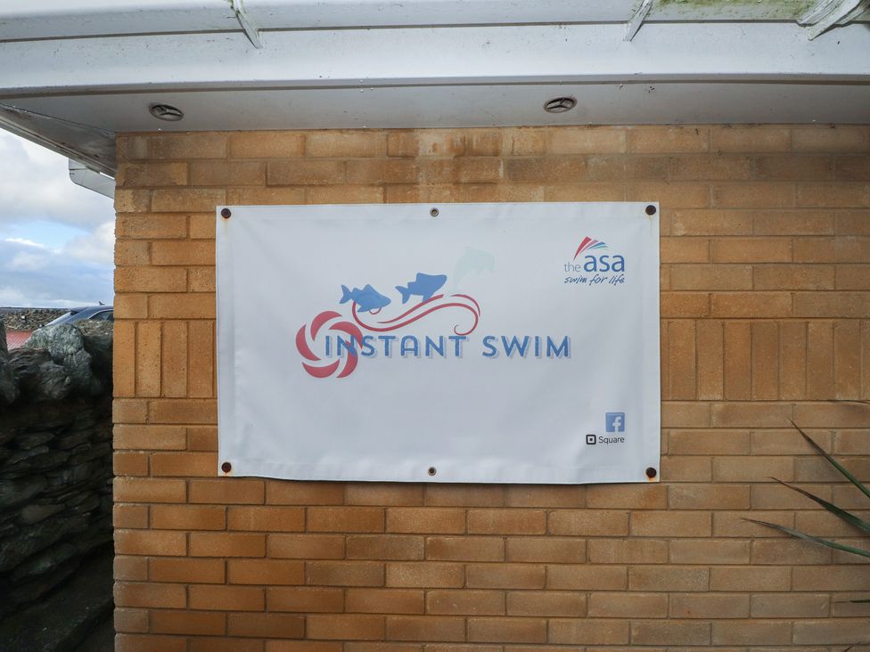 A banner displaying 'INSTANT SWIM' on a brick wall at King Arthur Suite Trearddur Bay