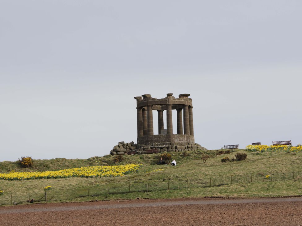 A monument with columns on a grassy hill with flowers and benches nearby at 9A Market Square
