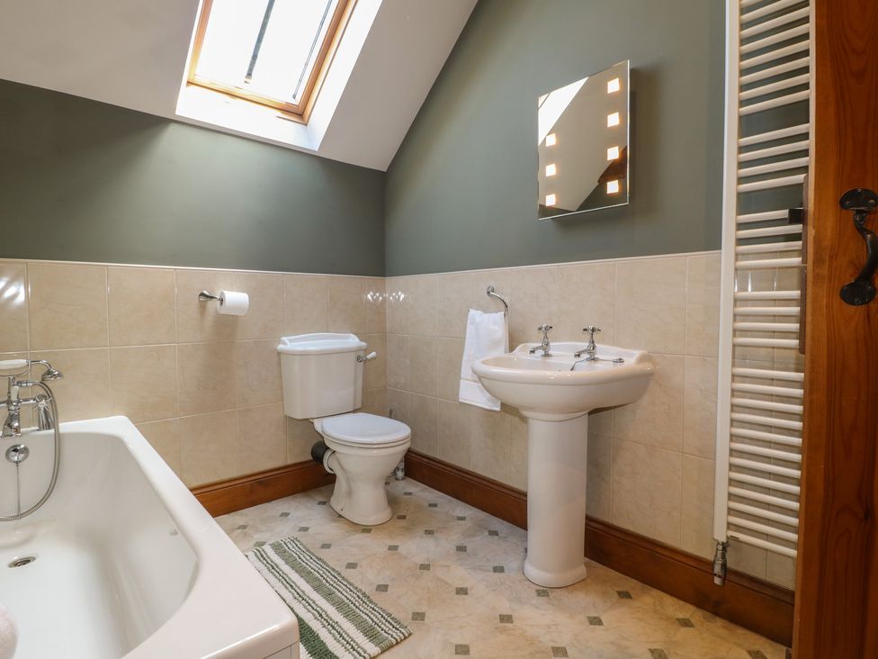 A bathroom with bathtub, toilet, sink and mirror at Carr House Farm in Waberthwaite