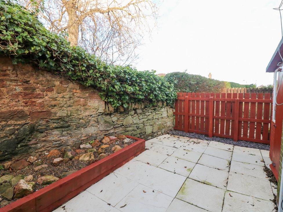 A garden with a stone wall and a fenced area at Seaspray in Beadnell
