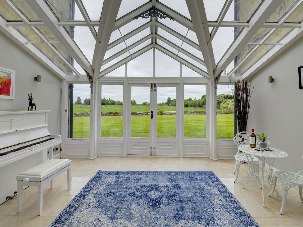 A conservatory with a piano and seating area at The Farm House in Aldbrough St. John near Barton