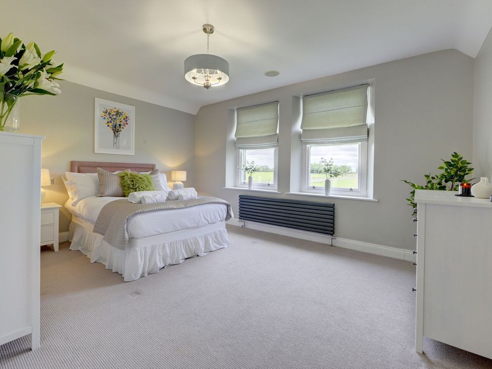 A bedroom with a bed and windows at The Farm House in Aldbrough St. John near Barton