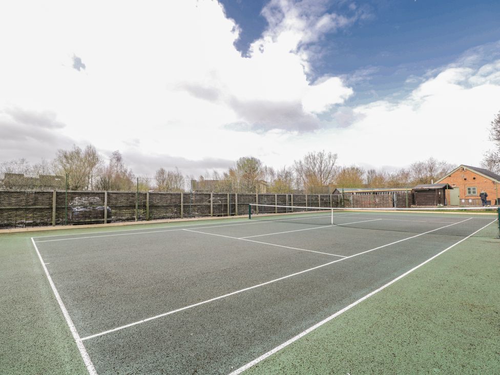 A tennis court with a net and surrounding buildings at Firefly Cottage 