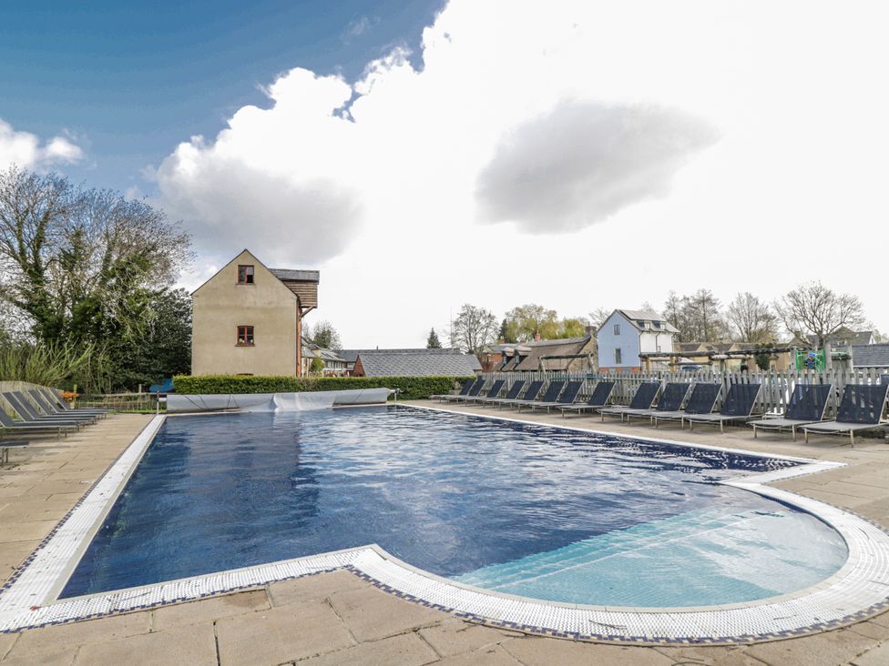 A swimming pool with loungers and buildings at Firefly Cottage