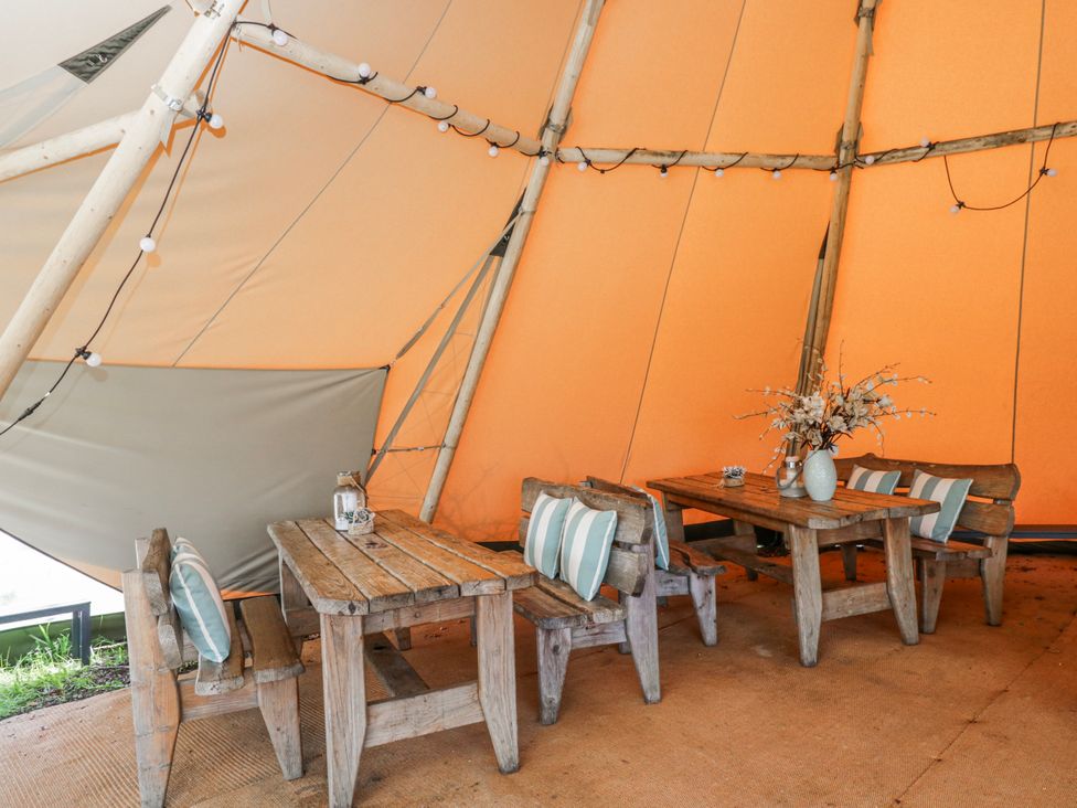 A tent interior with wooden tables and chairs at Firefly Cottage