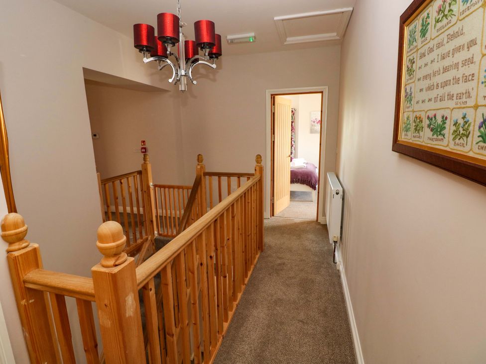 A hallway with a staircase and chandelier at The Sycamores in Llawhaden near Narberth