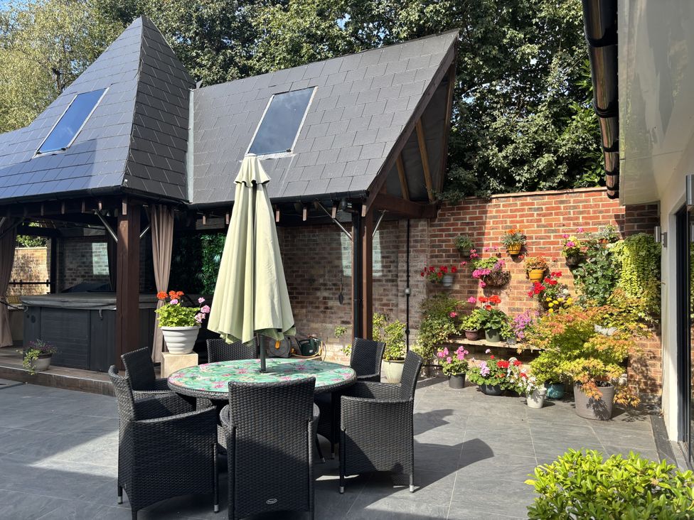 An outdoor area with a table and chairs, a hot tub, and a flower wall at 8 Church Road, Ferndown