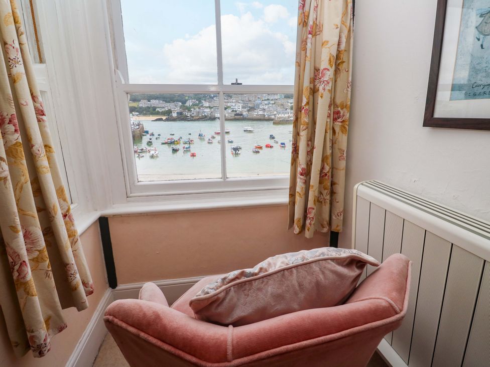 A chair near a window with curtains and a view of the harbor at Pelican Cottage in St Ives