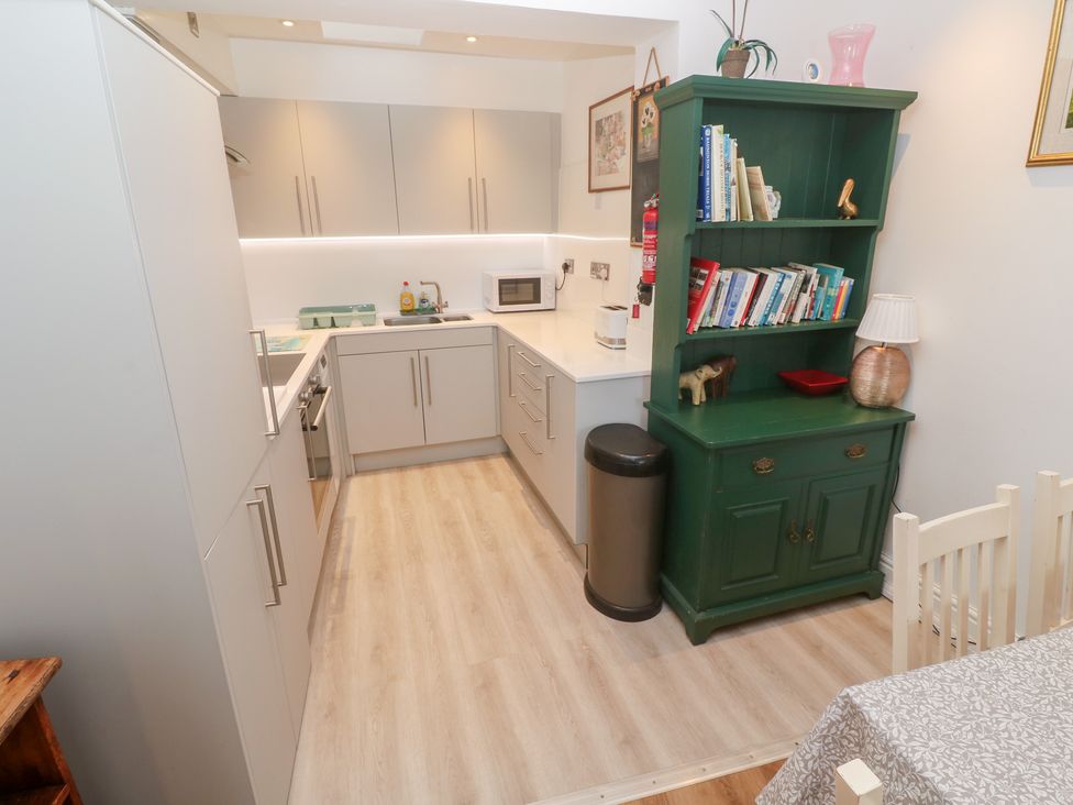 A kitchen with cabinets and a green bookshelf at Pelican Cottage in St Ives