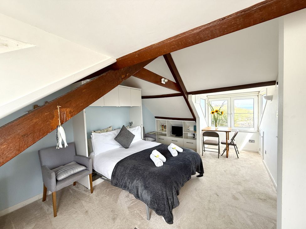 A bedroom with a bed, chair, and table at Crows Nest, St Ives
