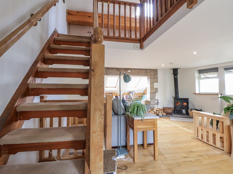 A living room with a staircase and wood stove at The Hayloft in Bodelwyddan