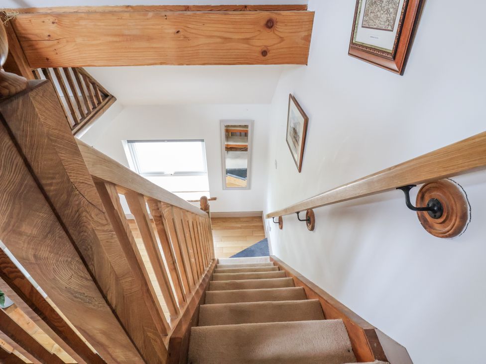 A staircase with wooden handrail and wall mirror at The Hayloft in Bodelwyddan