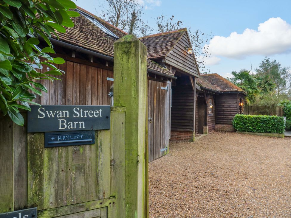 A sign at Swan Street Barn with surrounding buildings and gravel path at The Hayloft in Charing