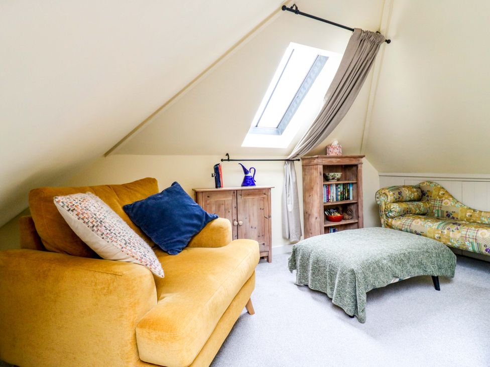 A snug with an armchair, sofa, and bookshelf at The Hayloft in Charing
