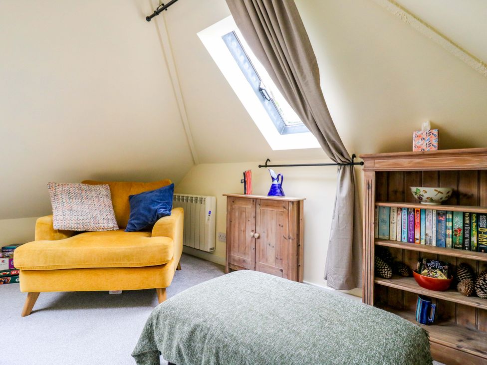 A snug room with a chair and bookshelf at The Hayloft in Charing