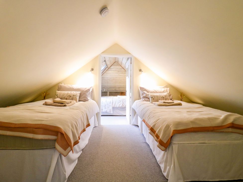 A bedroom with two beds and a door leading to another room at The Hayloft in Charing