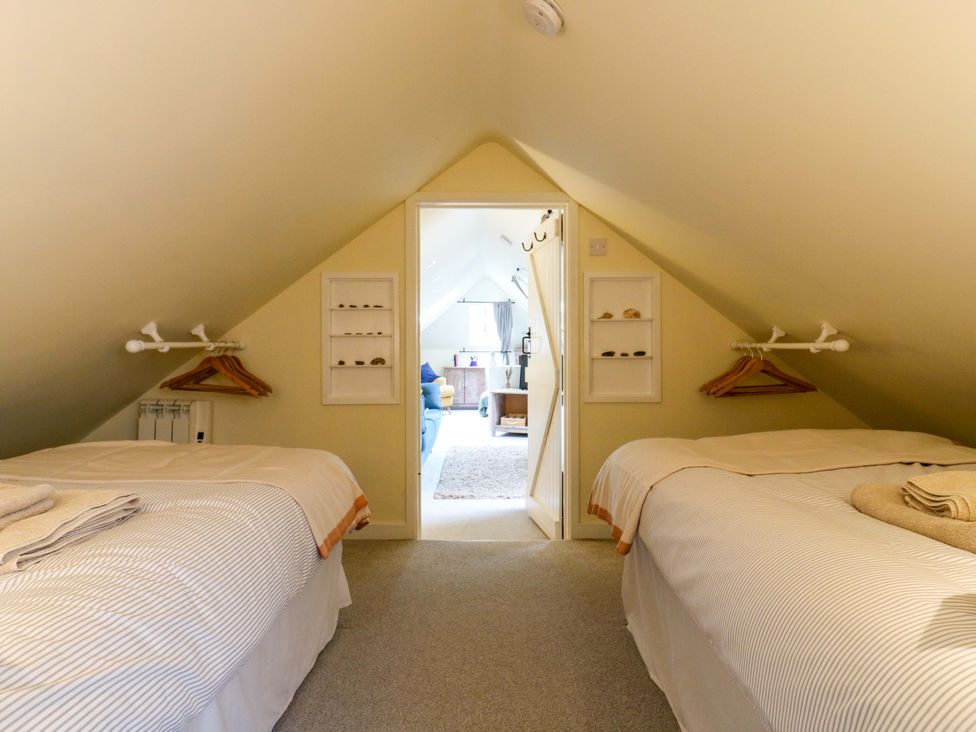 A bedroom with twin beds and a door leading to another room at The Hayloft in Charing
