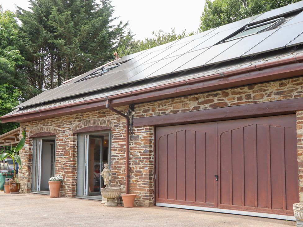 An exterior view of a building with a stone wall and solar panels at Tigley Meadow Coach House in Totnes