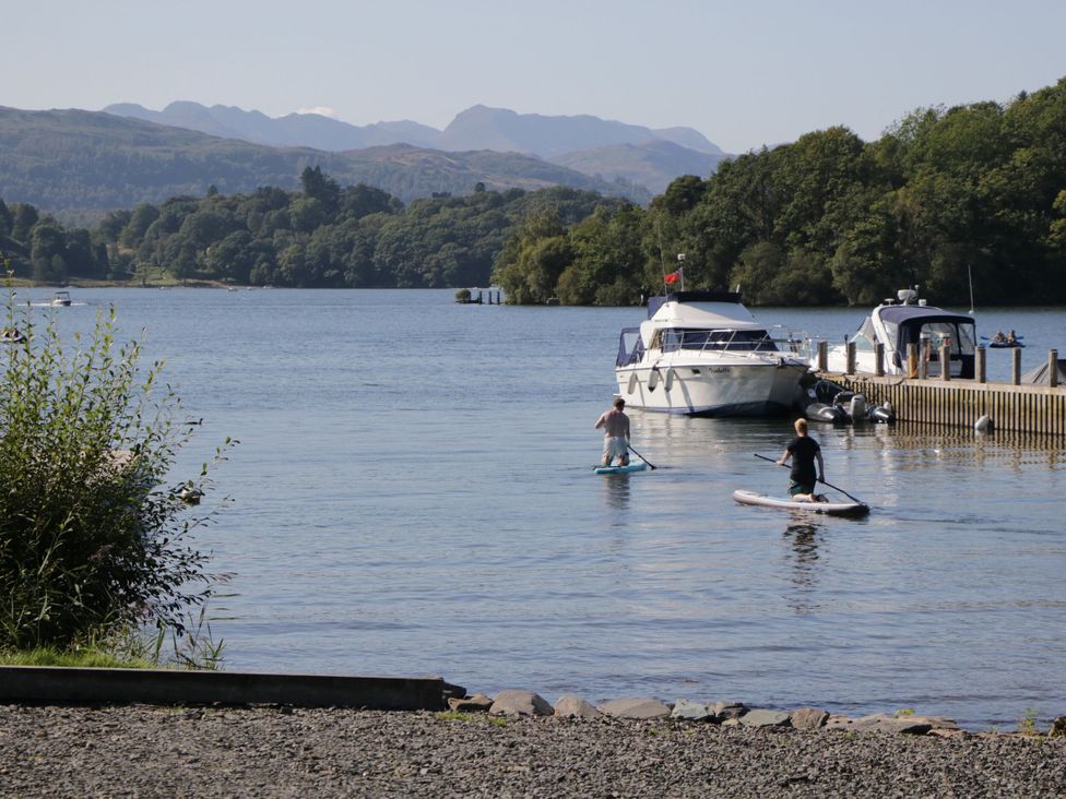 Two paddleboarders on the water with boats and mountains in the background at School Cottage, Troutbeck Bridge near Windermere