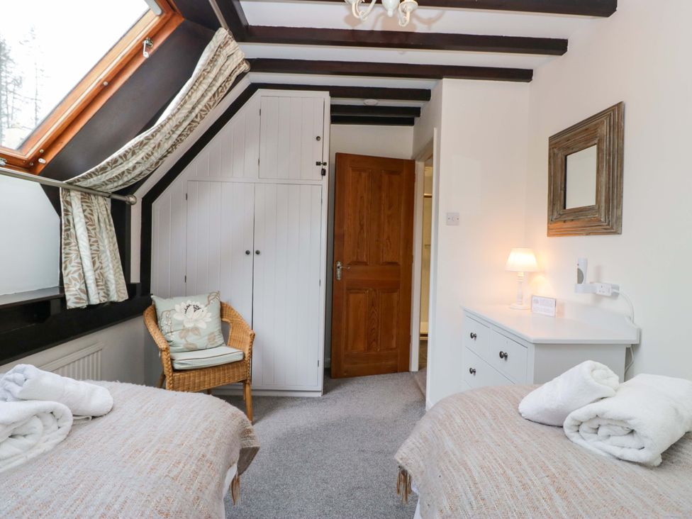 A bedroom with two beds and a wardrobe at School Cottage in Troutbeck Bridge near Windermere