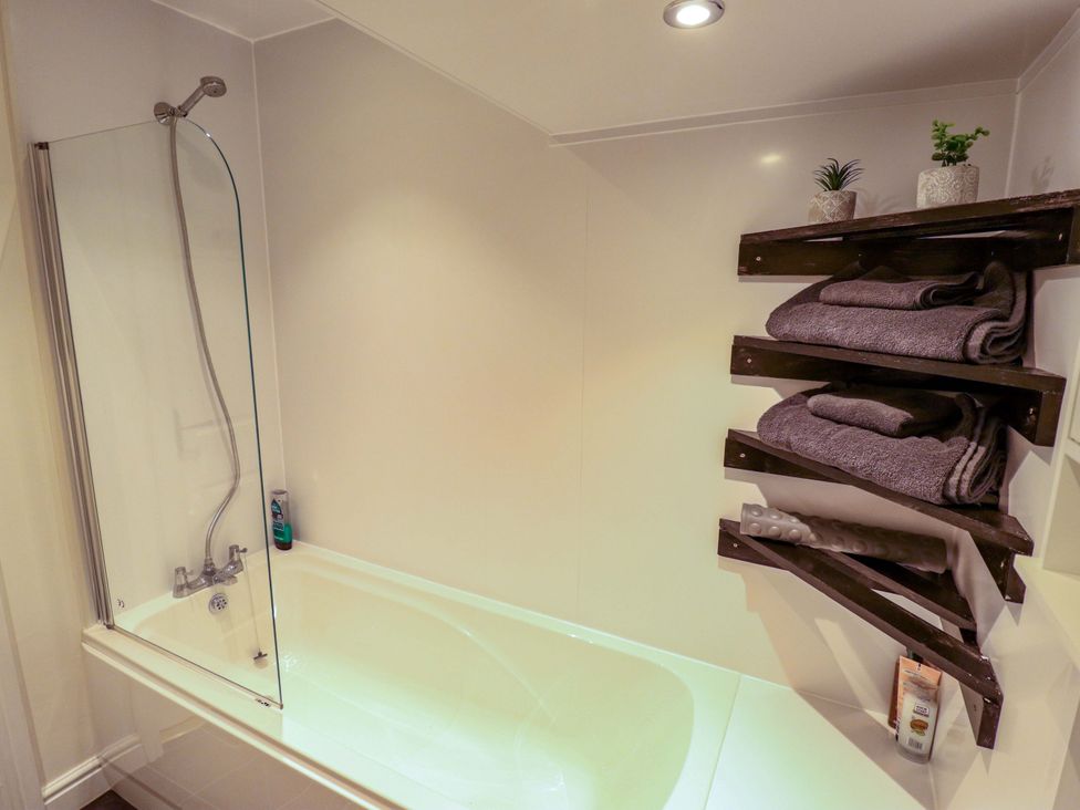 A bathroom with a bathtub and towels on shelves at 3 The Old Drill Hall Alford