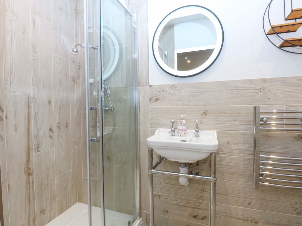 A bathroom with a shower, sink, and mirror at Gowan Brae in Criccieth