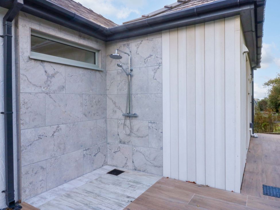 An outdoor shower area with a stone wall and a drain at Gowan Brae in Criccieth