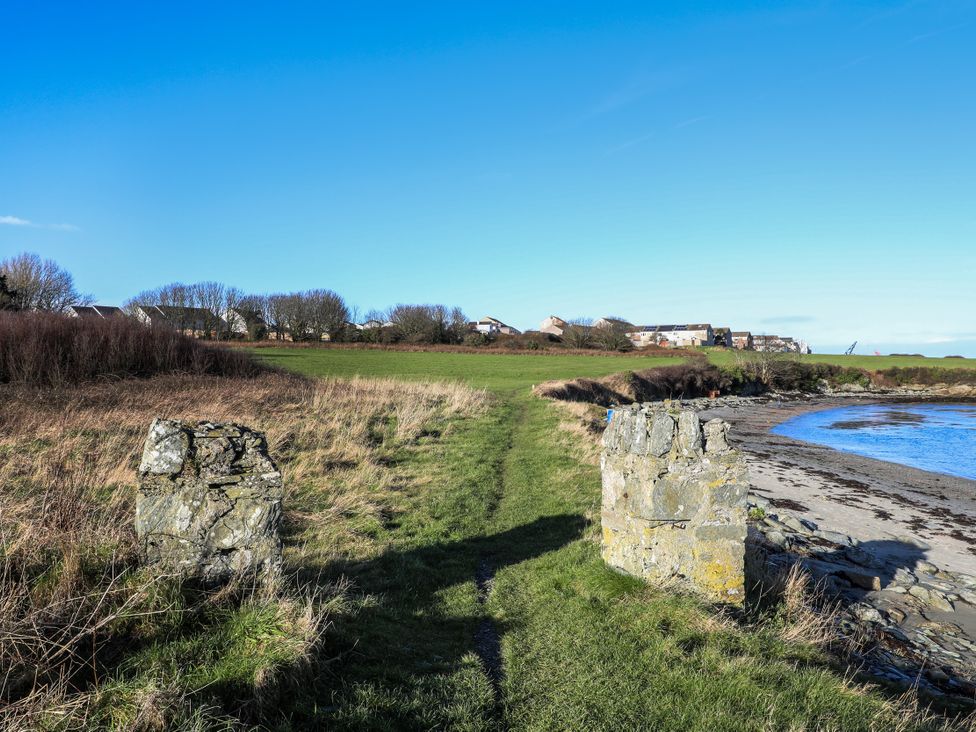 A pathway leading to water with ruins and houses in the background at Penrhos Walks in Holyhead