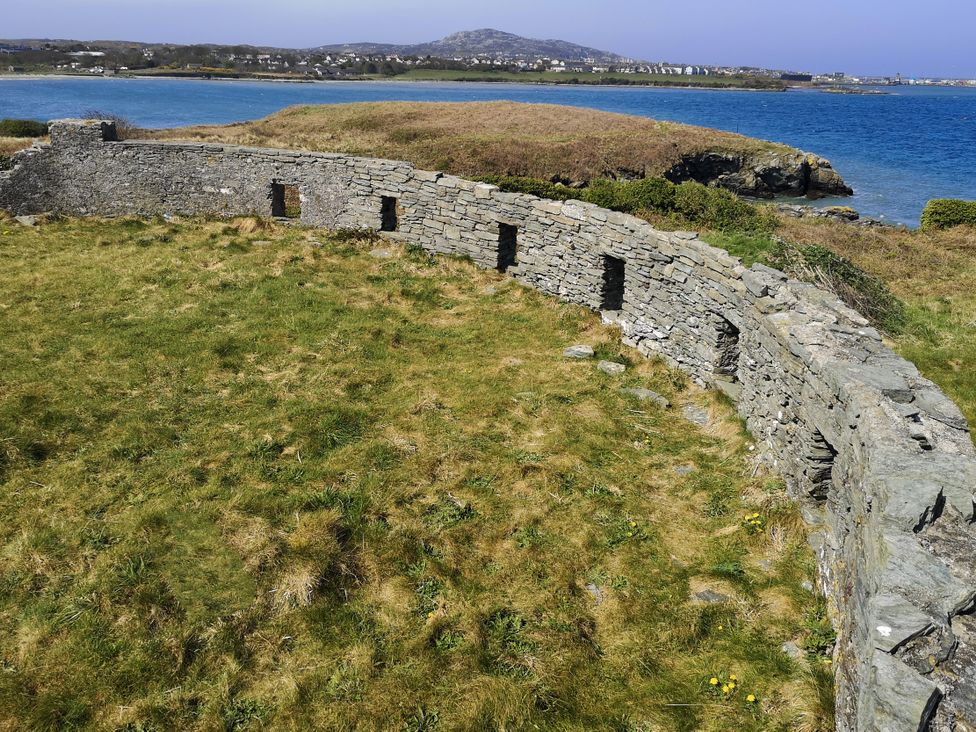 A stone wall with window openings and grass near water at Penrhos Walks Holyhead