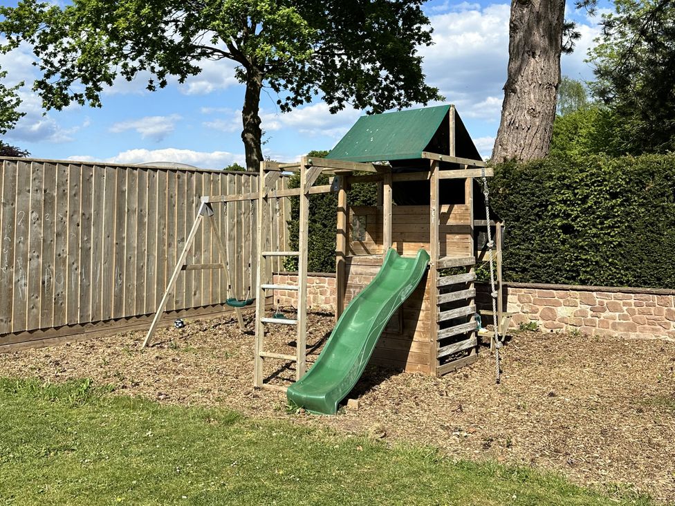 A playhouse with slide and swing set in a garden at The Old Vicarage 
