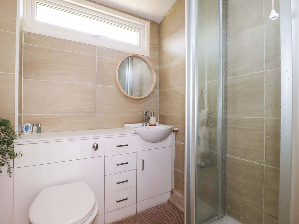 A bathroom with a sink, toilet, shower, and mirror at Cozy Retreat in Tregolds