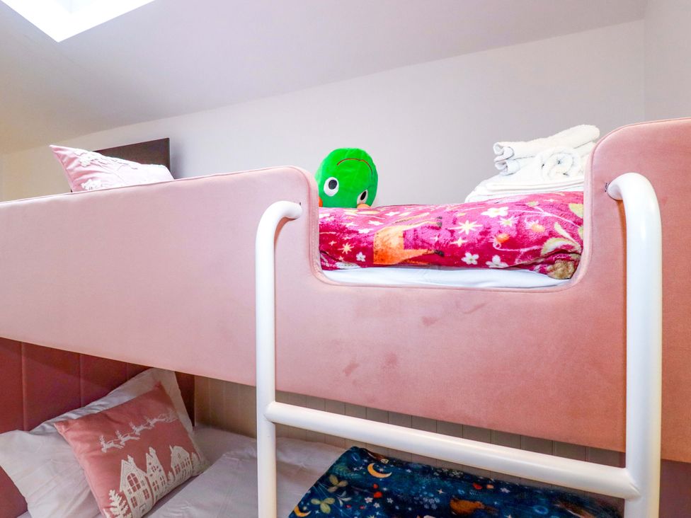 A bunk bed with a green plush toy and blankets at Ocean Edge in Sennen Cove