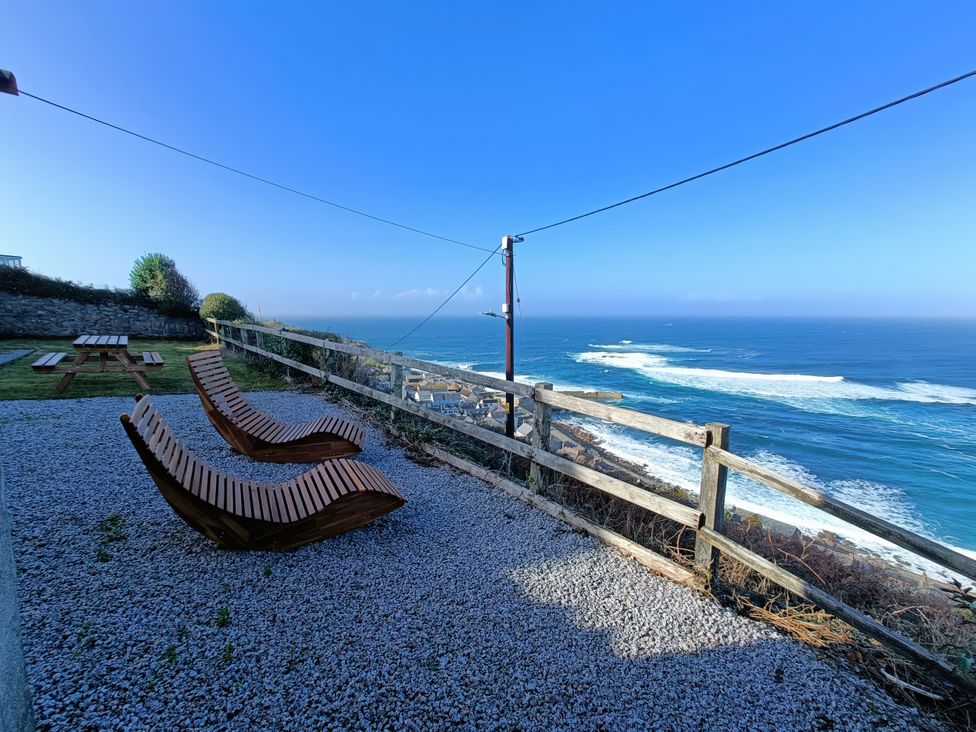 An outdoor area with wooden loungers and a picnic table at Ocean Edge Sennen Cove