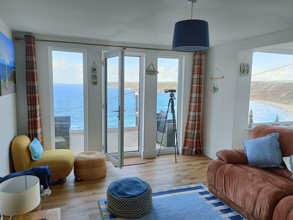 A living room with a sofa and windows overlooking the sea at Ocean Edge Sennen Cove
