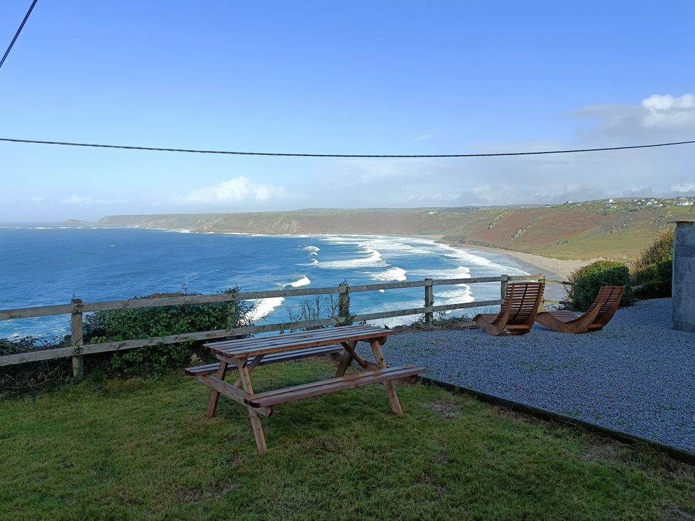 An outdoor area with a picnic table and deck chairs overlooking the ocean at Ocean Edge in Sennen Cove