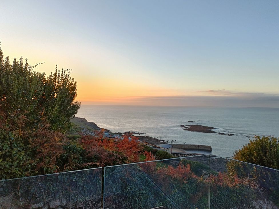 A view of the ocean and sunset with plants and rocks at Ocean Edge Sennen Cove