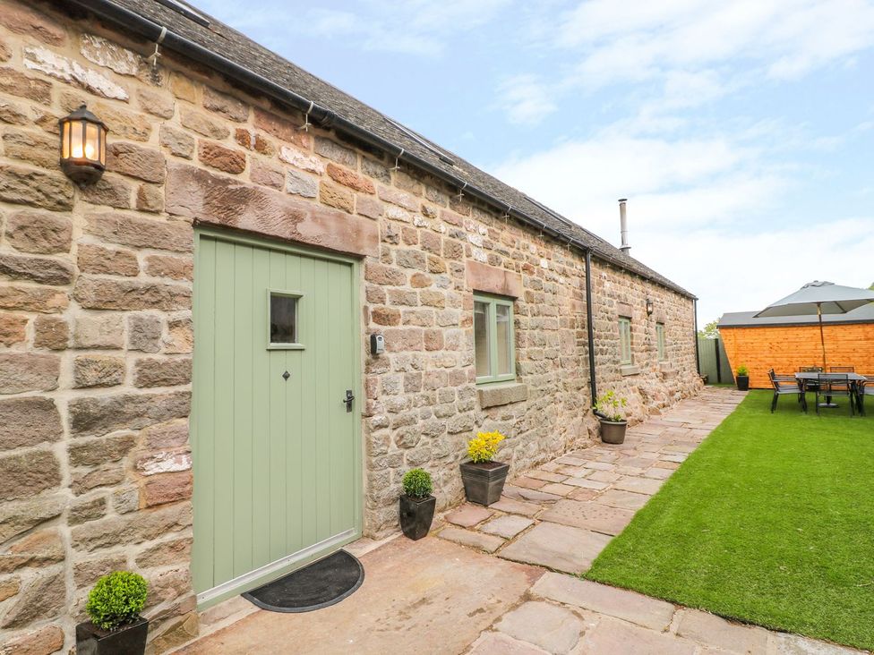 An outdoor area with a stone wall, green door and seating at The Barn in Wirksworth
