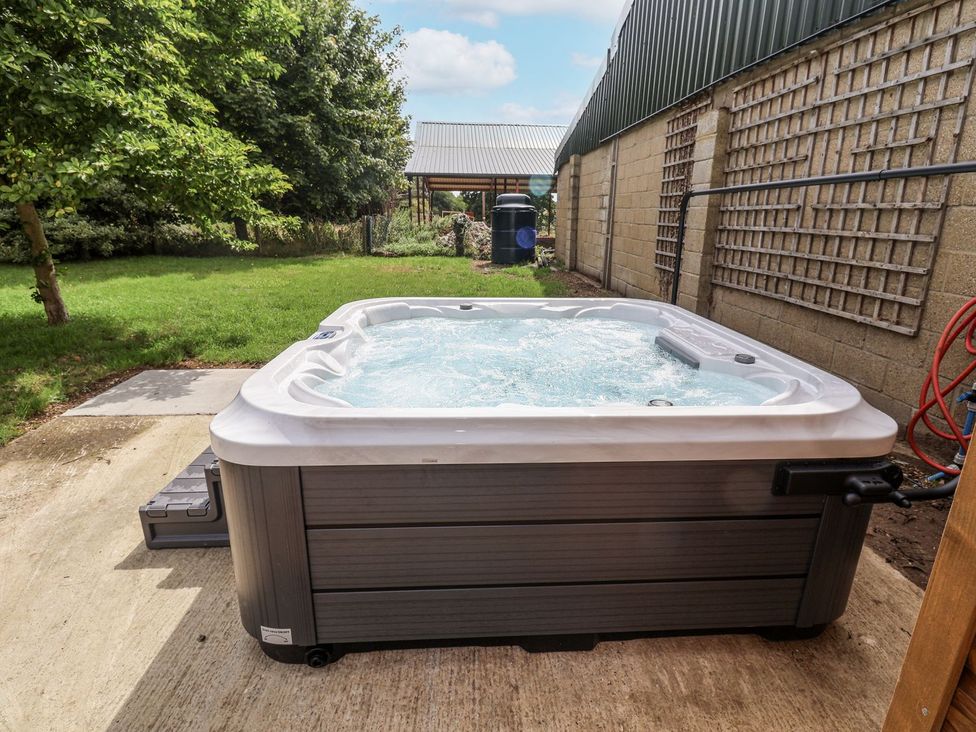 A hot tub on a patio with grass and a fence at Holly Farm near Brantham