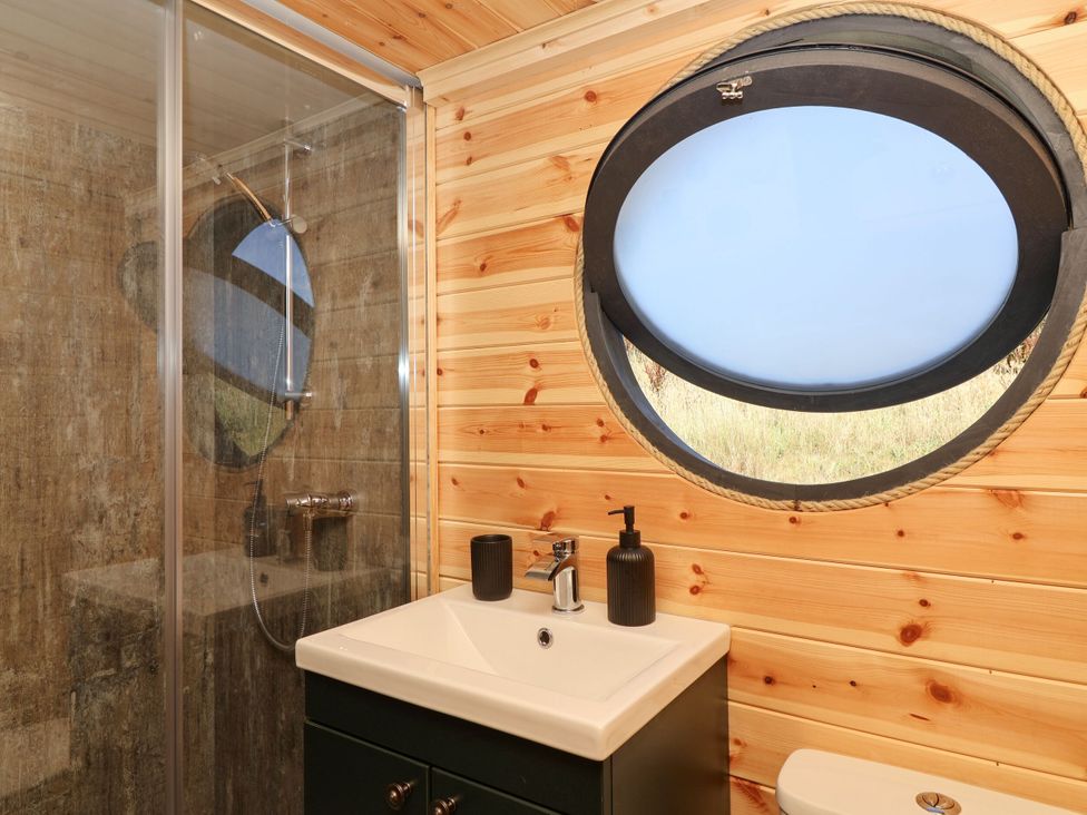 A bathroom with a shower, vanity sink, and round window at Bugley Pools Hideaway in Bugley near Gillingham