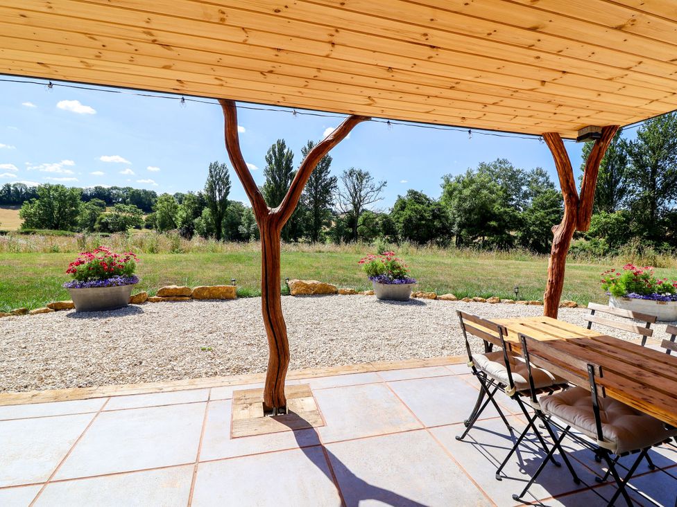 A patio with a table and chairs overlooking a grassy area at Bugley Pools Hideaway in Bugley near Gillingham