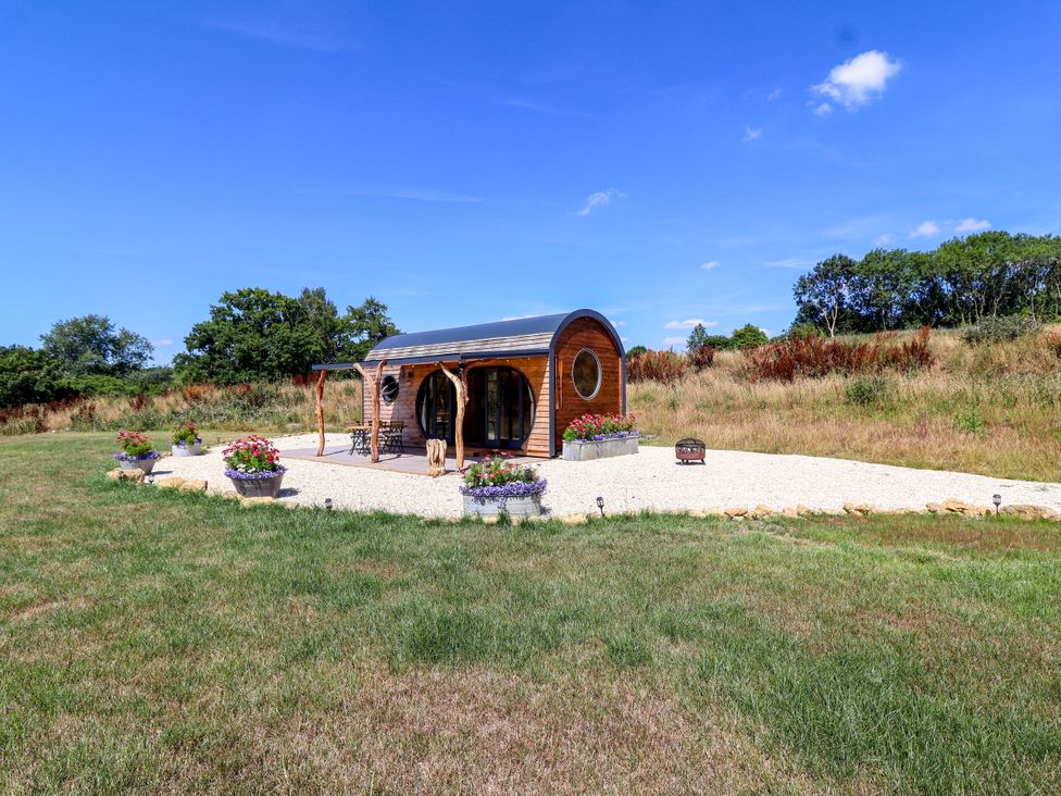 A cabin with flowers and a bench in an outdoor area at Bugley Pools Hideaway Bugley near Gillingham