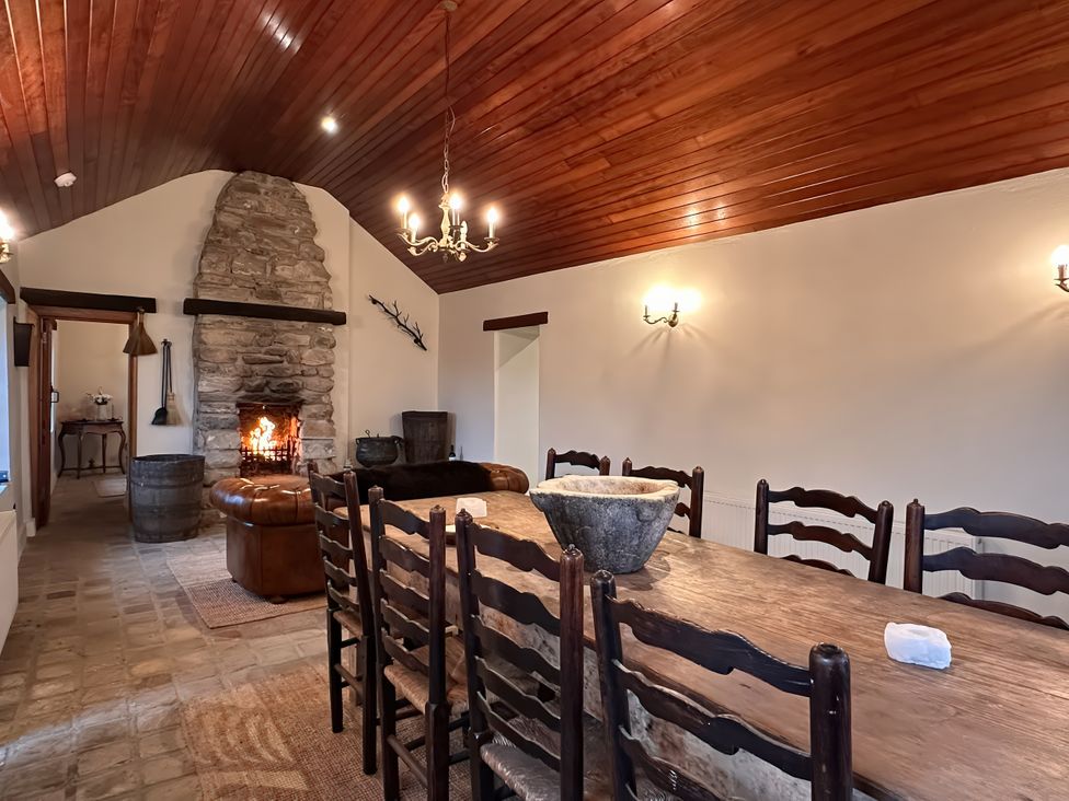 A dining room with a fireplace and wooden table at Cobble Stone Cottage near Leabgarrow, County Donegal