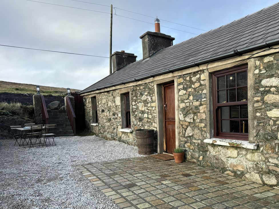 An outdoor view of a stone house with a table and barrel at Cobble Stone Cottage near Leabgarrow, County Donegal