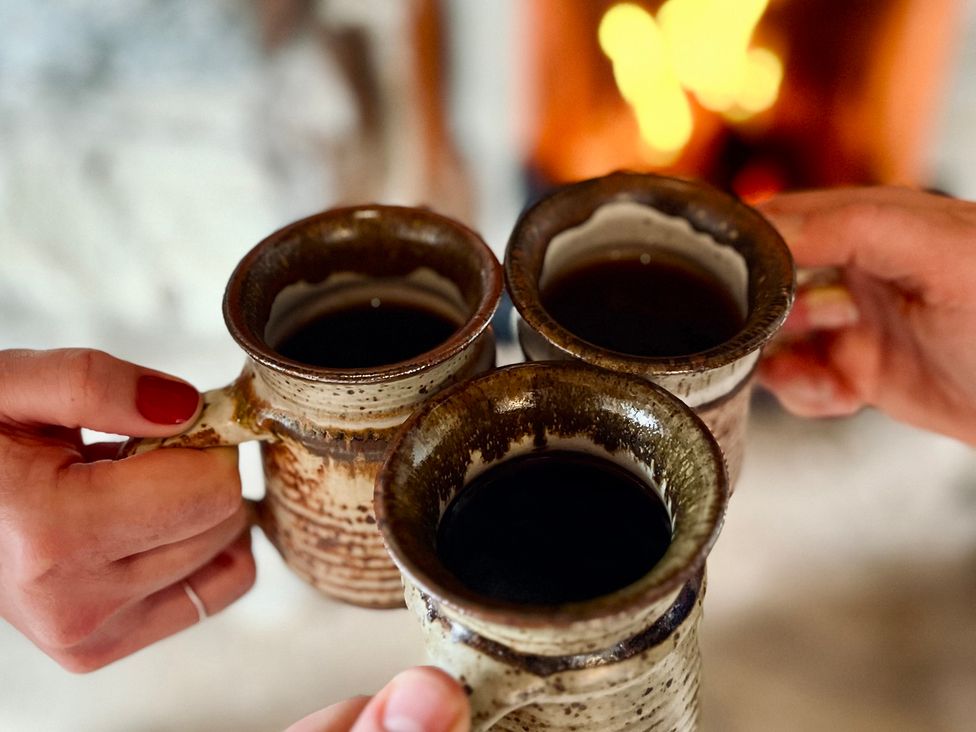 Three mugs with hot beverage held by hands near a fireplace