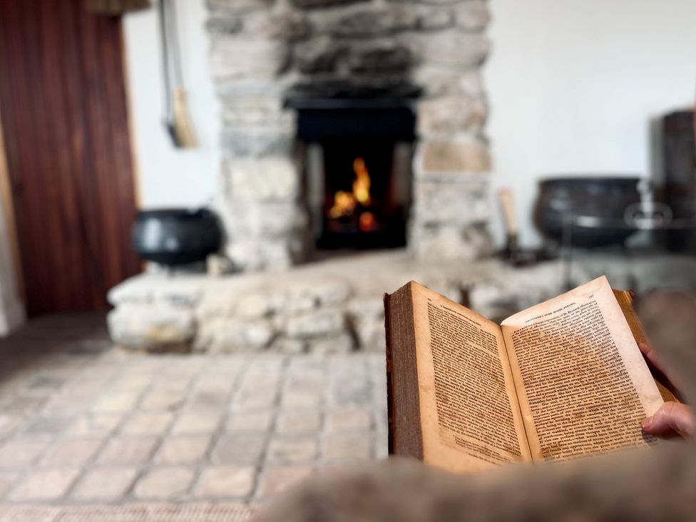 A living room with a fireplace and an open book at Cobble Stone Cottage near Leabgarrow, County Donegal