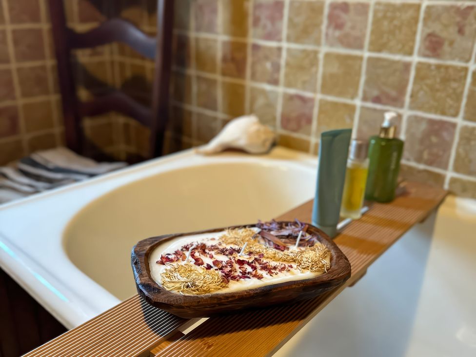 A bathtub with a wooden tray holding candles and bottles at Cobble Stone Cottage near Leabgarrow, County Donegal
