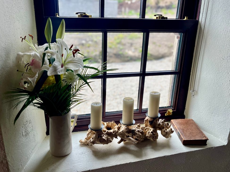 A window with flowers, candles, and a book at Cobble Stone Cottage near Leabgarrow, County Donegal