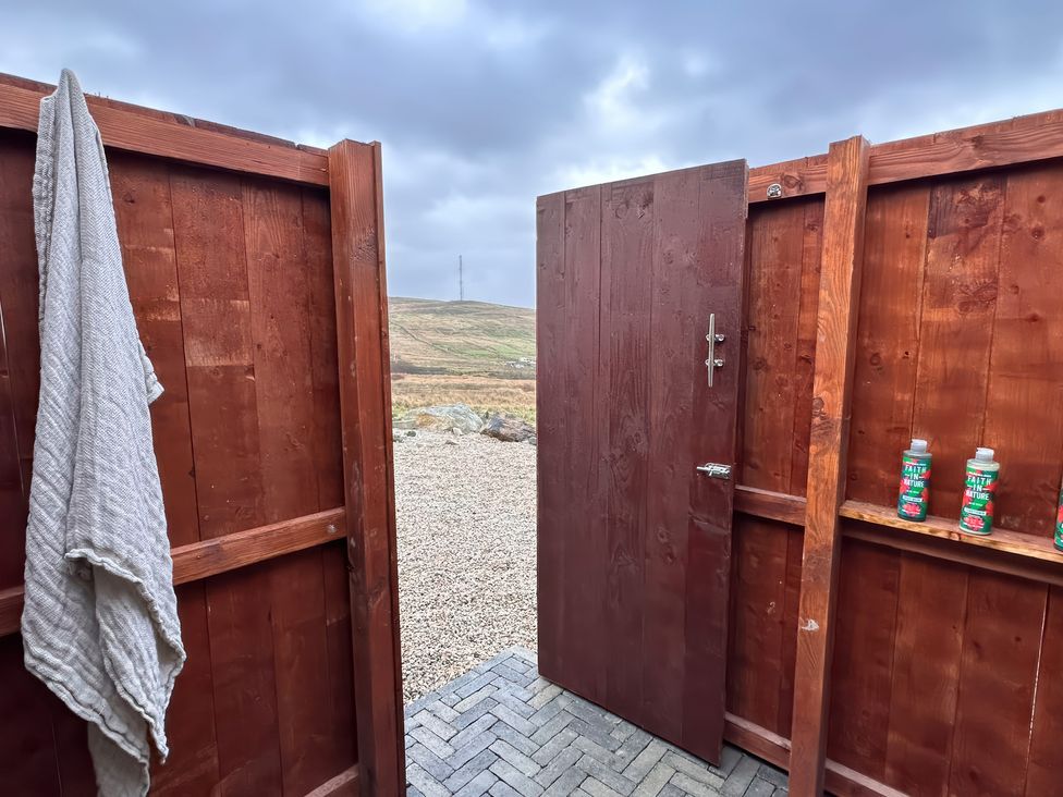 An outdoor shower area with a door open revealing bottles and a towel at Cobble Stone Cottage near Leabgarrow, County Donegal