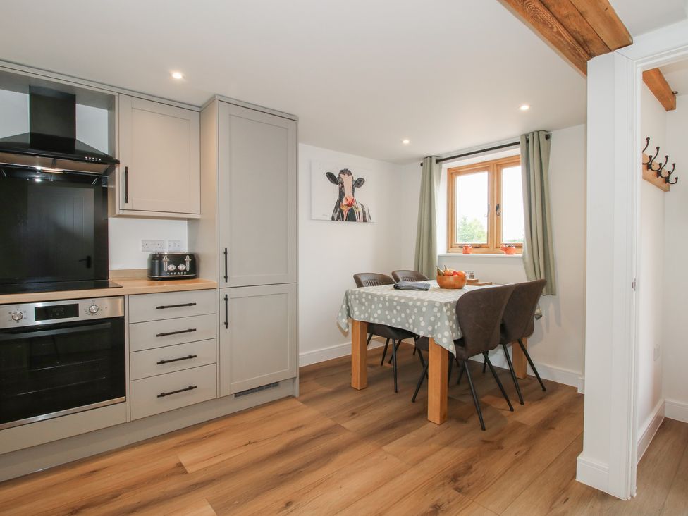 A kitchen with cabinets, oven, dining table, and window at Ash Barn Northwood near Wem